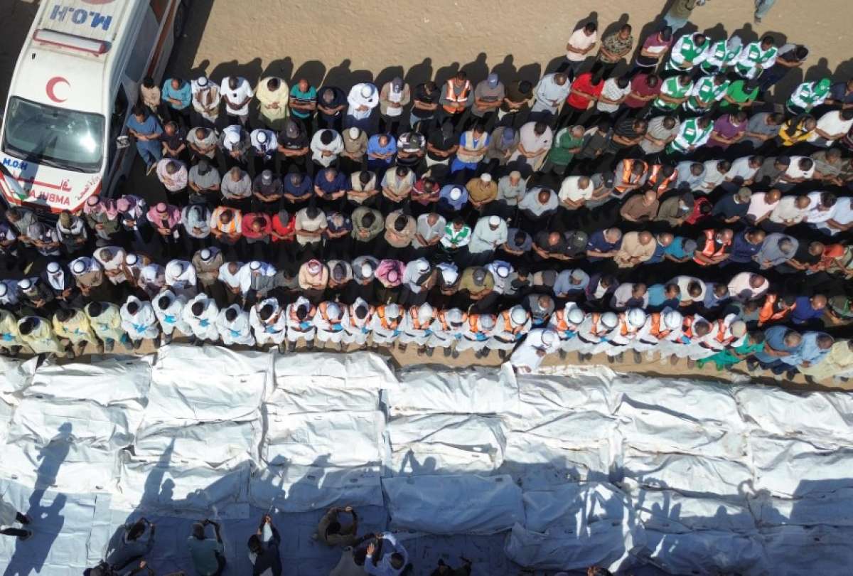 Equipos médicos rezan junto a los restos y cuerpos de palestinos no identificados, devueltos por Israel, antes de su entierro masivo fuera del Hospital Nasser en Khan Yunis, Franja de Gaza sur, 22 de octubre de 2025.